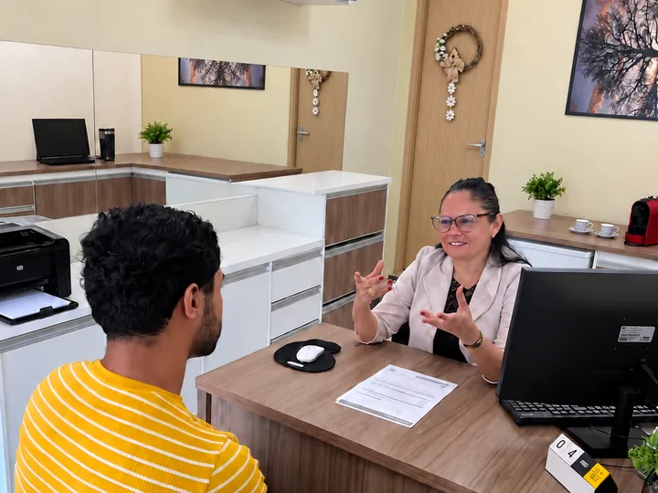 Suzane Salvador atendendo um cliente à mesa do escritório, explicando um documento